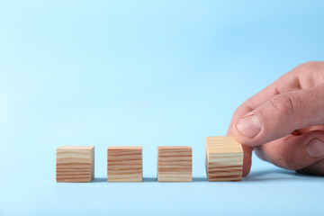 Man with wooden cubes on light blue background, closeup. Space for text