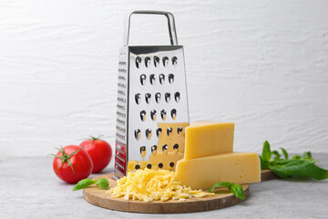 Grater, tomatoes, basil, grated and pieces of cheese on light table