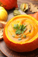 Tasty pumpkin cream soup with seeds and parsley served in pumpkin on wooden table, closeup
