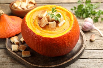 Tasty pumpkin cream soup with croutons and parsley served in pumpkin on wooden table, closeup