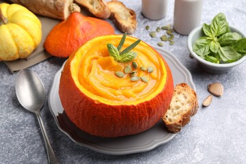 Tasty pumpkin cream soup with seeds and basil served in pumpkin on grey table, closeup