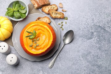 Tasty pumpkin cream soup with seeds and basil served in pumpkin on grey table, flat lay. Space for text