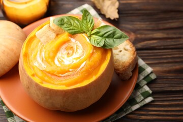 Tasty pumpkin cream soup with basil and croutons served in pumpkin on wooden table, closeup