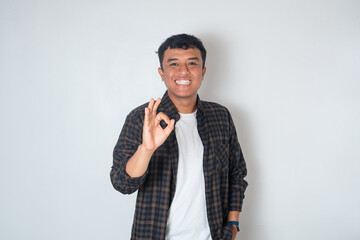 Smiling young Asian man in casual shirt doing ok sign with fingers isolated on white background