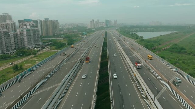 Aerial view of the expansive Dwarka Expressway featuring light vehicle traffic, flanked by buildings and a serene water body, Gurugram, Haryana, India.