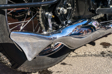 Chrome exhaust and rear wheel of a vintage motorcycle with drive chain, retro-style mechanical detail captured at a classic vehicle rally