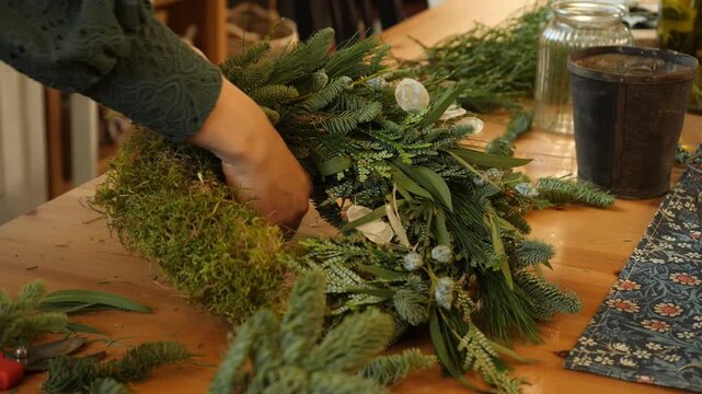 Hands assembling Christmas wreath of pine, olive leaves, and moss