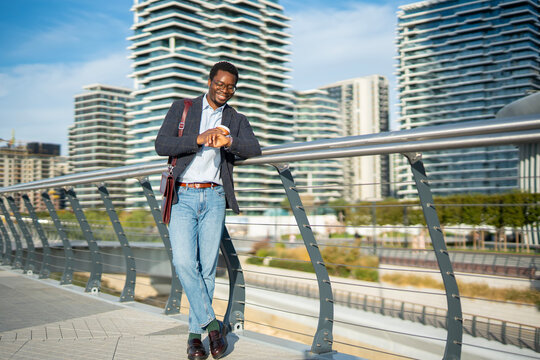 Young black businessman checking smartwatch on urban bridge