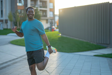 Happy black man stretching leg before running outdoors