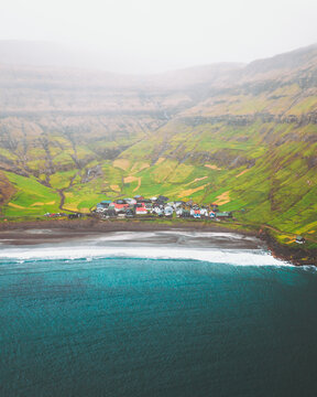 Aerial view of the village nestles between the dark beach and the verdant hillsides, a palette of nature's artistry under a misty sky, Tj&Atilde;&cedil;rnuv&Atilde;&shy;k, Streymoy, Faroe Islands.