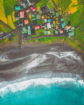 Aerial view of a village perched between verdant hills and a dramatic black sand beach where turquoise waves crash, Tj&Atilde;&cedil;rnuv&Atilde;&shy;k, Streymoy, Faroe Islands.