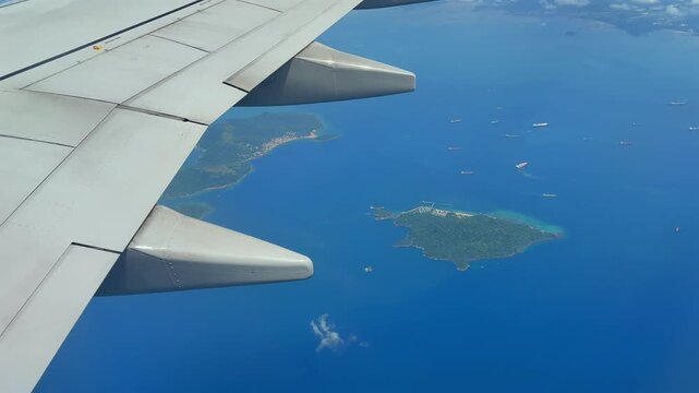 Airplane wing view over tropical blue sea with lush Panama island archipelago and cargo ships below