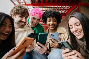 Diverse group of students are sitting together, enjoying funny social media videos on campus stairs. College lifestyle and youth community concept.
