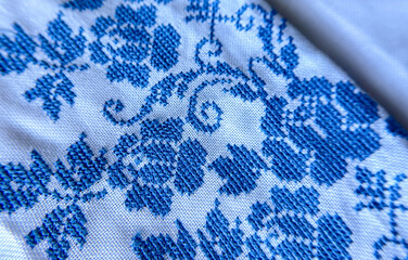 A close-up macro shot of traditional blue embroidery on a white linen fabric.