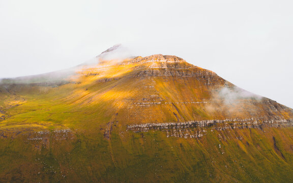 Aerial view of a majestic mountain shrouded in mist, its slopes painted with vibrant greens and earthy browns, Sl&Atilde;&brvbar;ttaratindur, Eysturoy, Faroe Islands.
