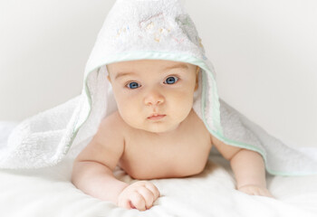 Cute baby with blue eyes under a soft towel. Baby wrapped in a towel after bath time.