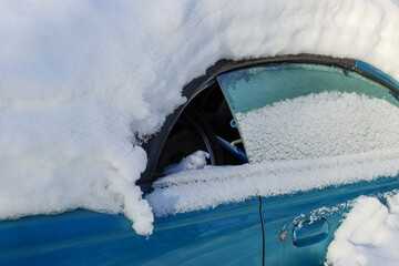 An abandoned car covered in snow in a parking lot in Espoo in January 2024. The window of a blue...