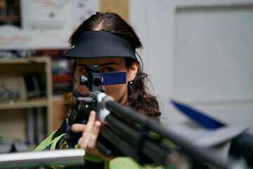 Focused woman aiming a rifle, precision shooting sport, competitive marksman, indoor range,...