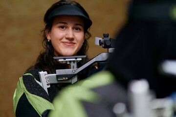 Female rifle shooter aiming, focused on target, competitive sport, determination and precision,...