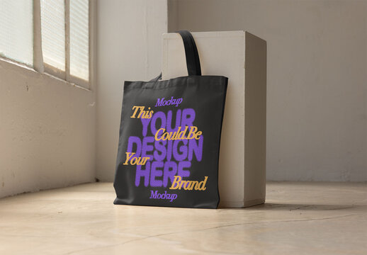 Tote bag rests against a white pedestal in a bright urban studio.