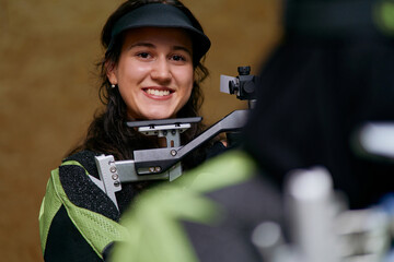Smiling woman aiming air rifle, indoor shooting range, professional sportswoman with rifle,...