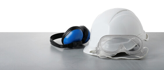 Safety equipment. Hard hat, earmuffs and goggles on gray table against white background