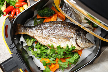 Air fryer with tasty grilled fish and vegetables on table, top view