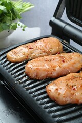 Electric grill with raw marinated chicken fillet on table against grey background, closeup