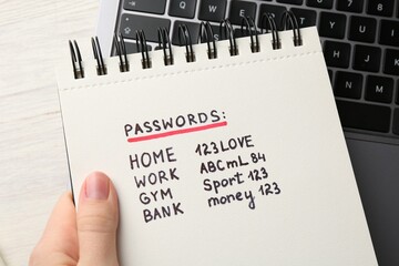 Woman holding notebook different passwords at table, closeup