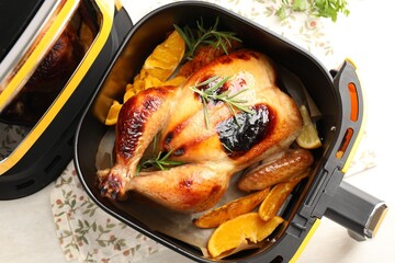 Tasty grilled chicken with rosemary in air fryer on white wooden table, top view