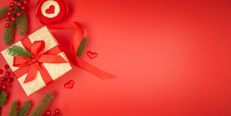 Christmas background with golden gift box and red ribbon on red backdrop, fir branches, berries and heart decorations, festive minimal composition with copy space for text, top view flat lay