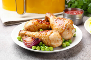 Grilled chicken drumsticks served with green peas on grey table, closeup