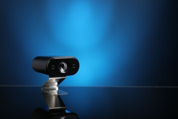 Modern hidden spy camera on mirror surface against blue background, closeup. Space for text