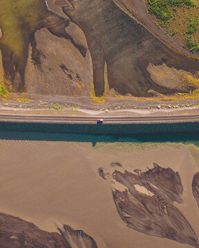Aerial view of a solitary car traversing a stark bridge, contrasting the textures of riverbed and the verdant land, Landeyjah&Atilde;&para;fn, Rang&Atilde;&iexcl;r&Atilde;&frac34;ing eystra, Iceland.