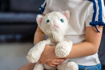 Child holding a well-worn plush toy tightly in both hands. Emotional connection to a beloved object that provides comfort, security, and a sense of familiarity in early childhood.