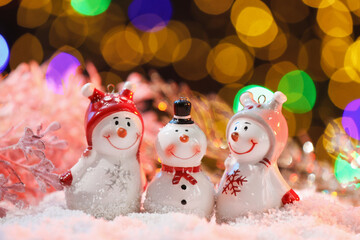 Cute decorative snowmen on artificial snow against blurred lights, closeup