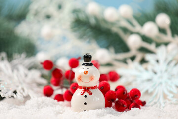 Cute decorative snowman, branch with red berries and snowflakes on artificial snow against blurred background, closeup