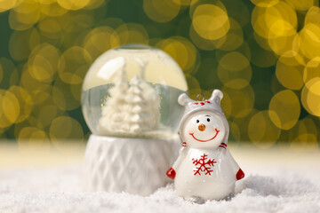 Cute decorative snowman and snowball on artificial snow against blurred lights, closeup