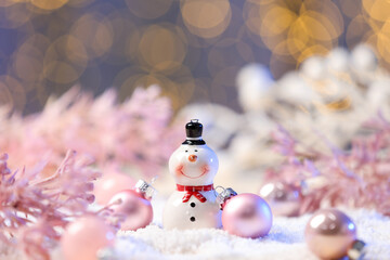 Cute decorative snowman, pink branches and baubles on artificial snow against blurred background, closeup