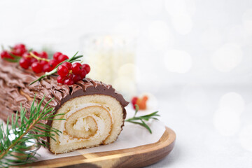 Delicious Yule log (traditional Christmas cake) with redcurrant and fir tree branches on light table, closeup. Space for text
