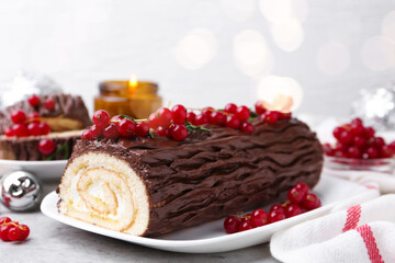Delicious Yule log (traditional Christmas cake) with redcurrant on gray textured table, closeup
