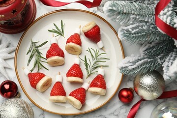 Christmas food. Santa hats made of marshmallows, strawberries, bananas, rosemary and decor on white marble table, flat lay