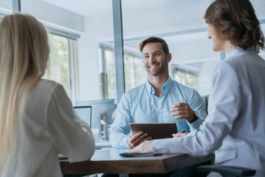 Young real estate manager worker man talking with bank client in office. Business meeting of busy entrepreneur people sitting at table, using gadget tablet device, discussing financial trade strategy