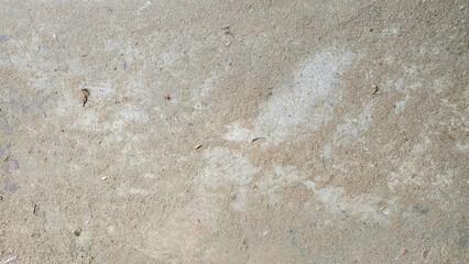 Close-up texture of an old concrete floor with light brown dust, cracks, and natural rough patterns showing worn and uneven surface details.