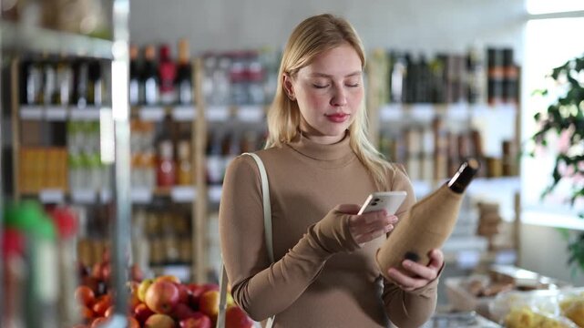 Young woman buyer scanning qr code for bottle of wine in grocery store