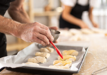 Baker's hands grease pieces of dough on baking sheet