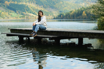 Brunette Woman Sitting on Pier by the Lake in Autumn
