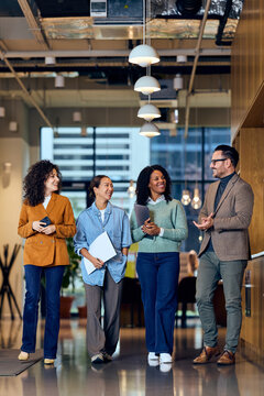 Diverse Team Of Colleagues Sharing Friendly Conversation In Modern Office Hallway During Casual Business Meetup