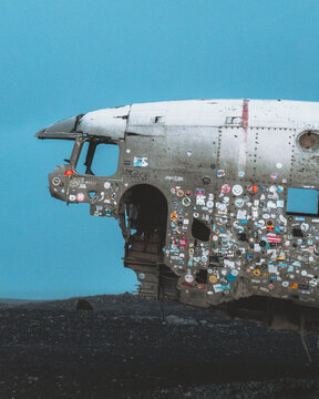 View of a weathered DC-3 plane wreck, adorned with stickers, sits starkly against the moody sky, a silent monument on the black sands, Solheimasandur Plane Wreck, Myrdalshreppur, Iceland.