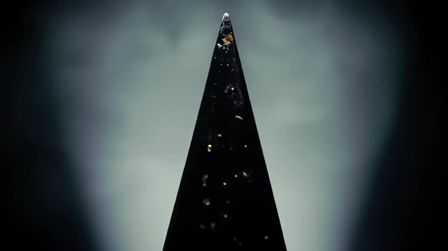 Abstract black pyramid shape with water droplets in spotlight